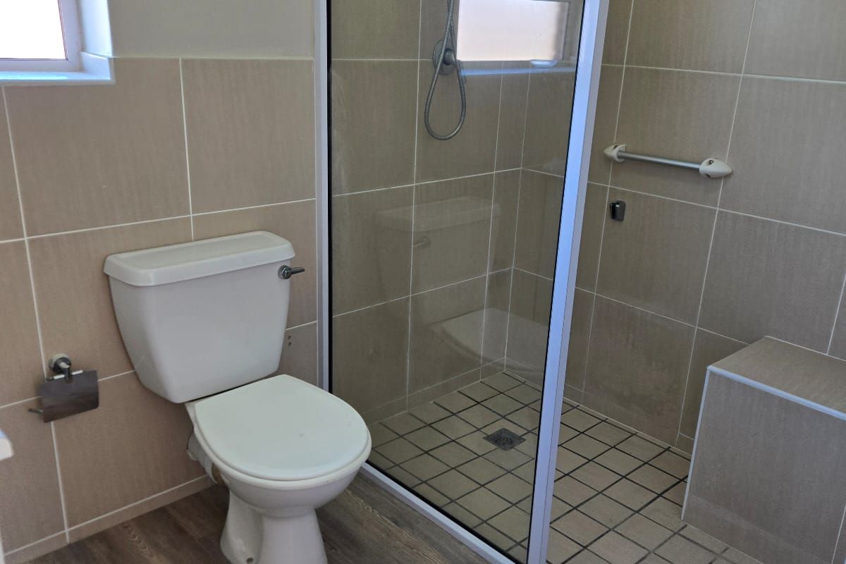 A clean bathroom featuring a walk-in shower with a built-in bench, glass enclosure, toilet, and wood-look flooring.