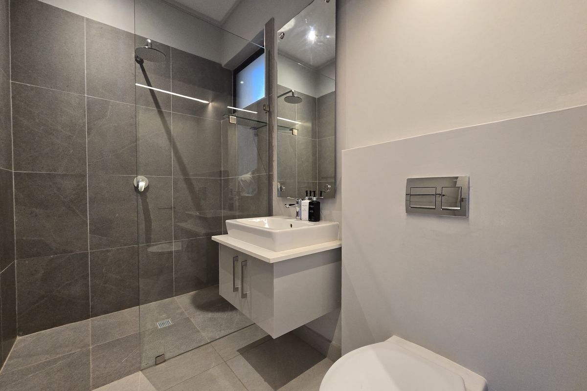 Modern bathroom featuring a walk-in shower with glass screen, wall-mounted vanity with basin, and a concealed cistern toilet with chrome flush plate.