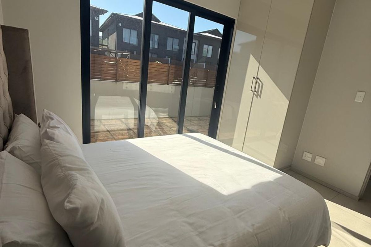 A modern bedroom featuring built-in high-gloss cabinetry, tiled flooring, recessed ceiling lighting, and large sliding glass doors leading to an outdoor area.