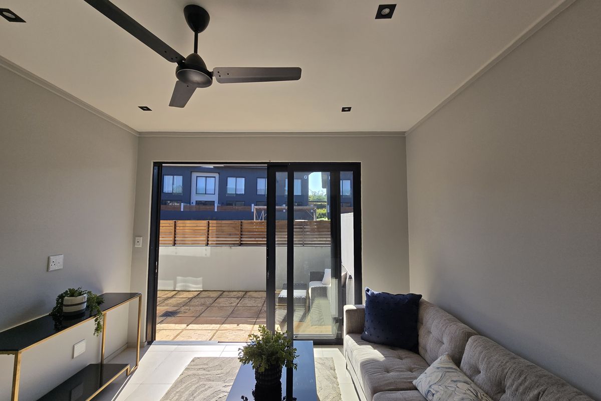 A bright living room featuring modern recessed lighting, a ceiling fan, and large sliding glass doors that open onto a private tiled patio.