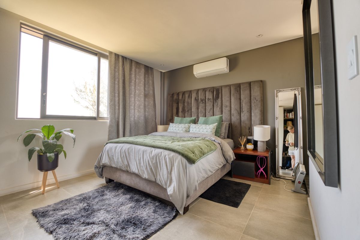 A well-maintained bedroom featuring large windows, tiled flooring, and a wall-mounted air conditioning unit.