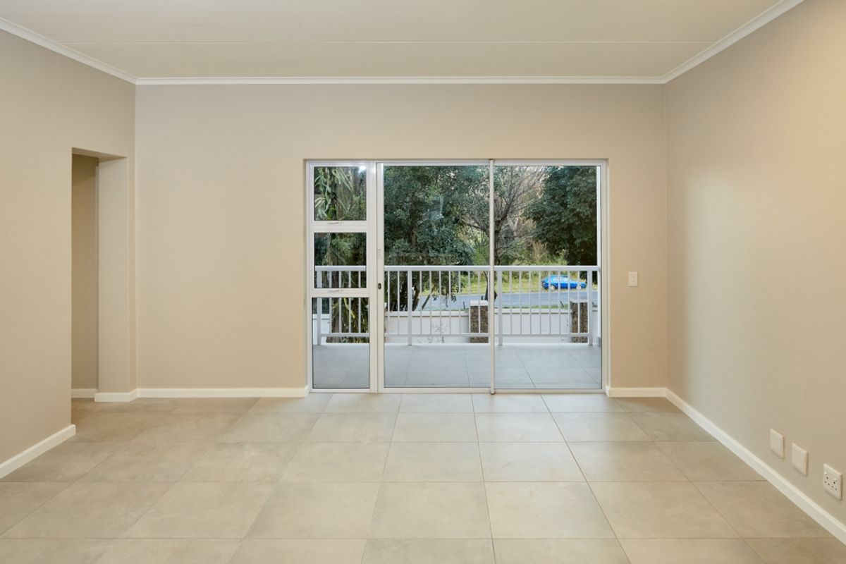 A bright, empty living area featuring neutral tiled flooring, coving, and a large sliding glass door providing access to a private balcony.