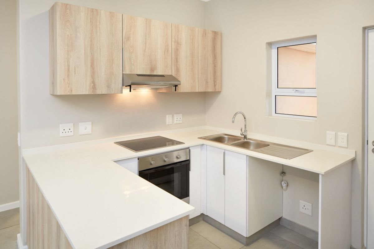 Modern kitchen featuring light wood-grain cabinetry, white stone countertops, integrated electric hob, oven, extractor fan, and a stainless steel double sink.