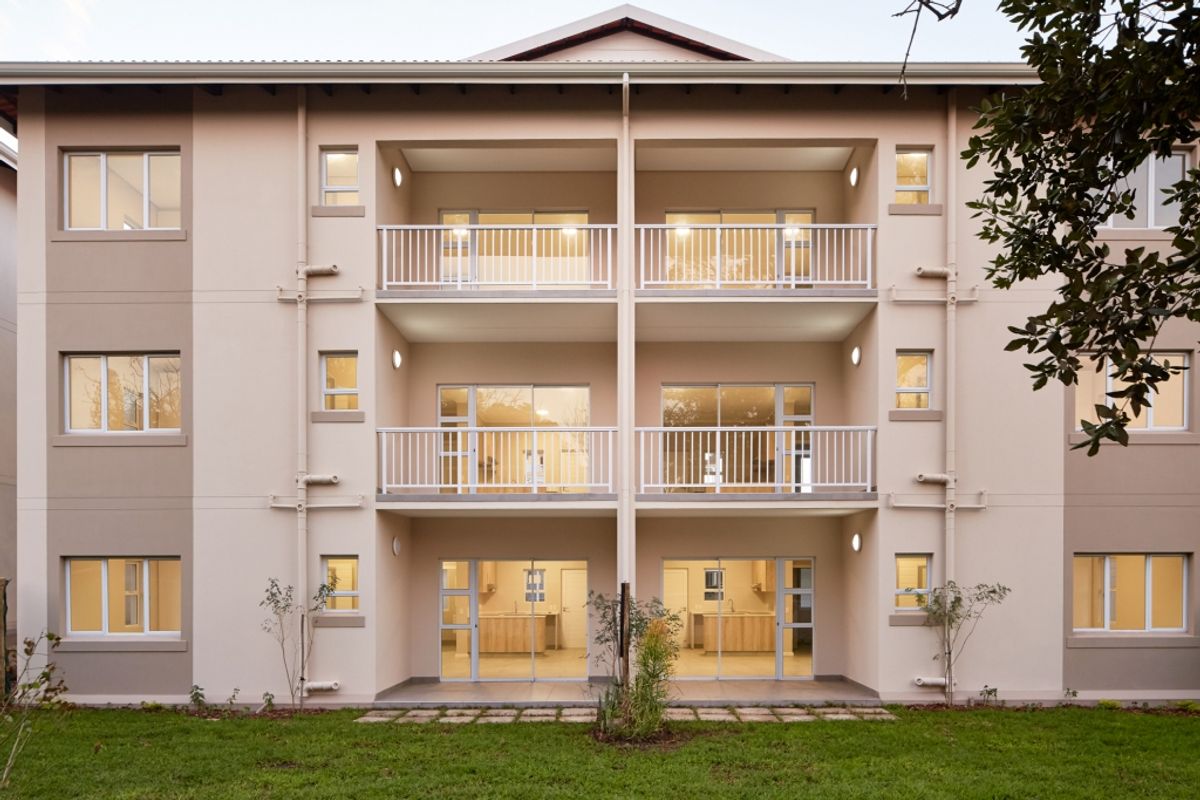 Rear elevation of a modern apartment building featuring multiple levels of balconies with white railings and ground-floor patio access.
