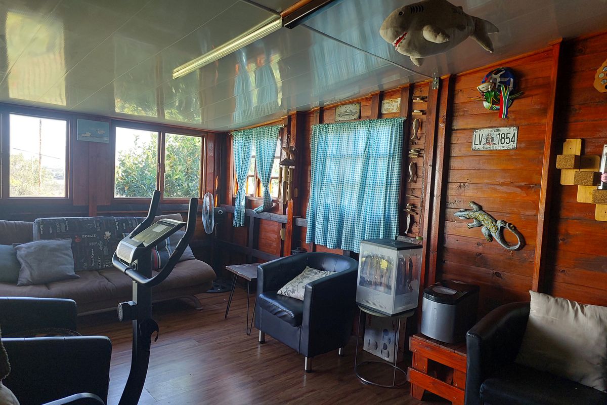 A rustic living space featuring timber-clad walls, laminate flooring, and large windows providing natural light.