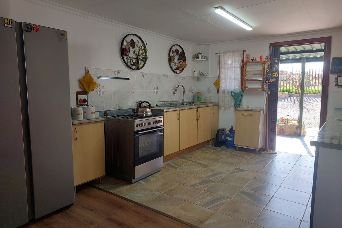 Functional kitchen featuring light wood cabinetry, tiled splashback, stainless steel stove, and direct access to the outdoor area.