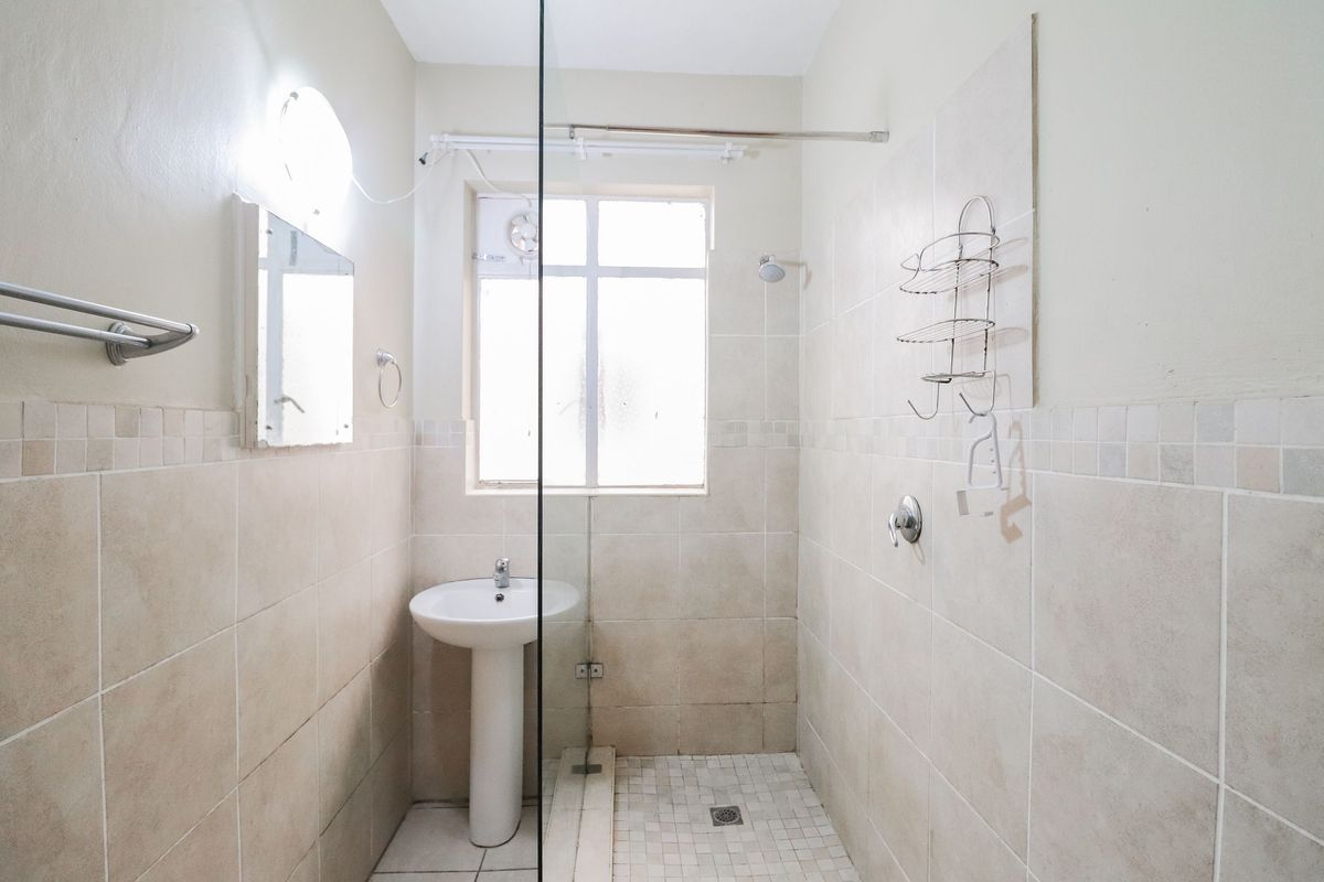 A functional bathroom featuring a pedestal sink, a glass-enclosed shower area with tiled walls, and a window for natural light.