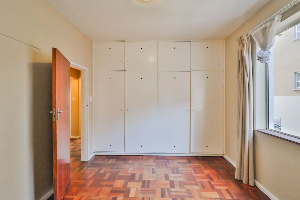 A bedroom featuring original parquet flooring and extensive floor-to-ceiling built-in storage cabinetry.