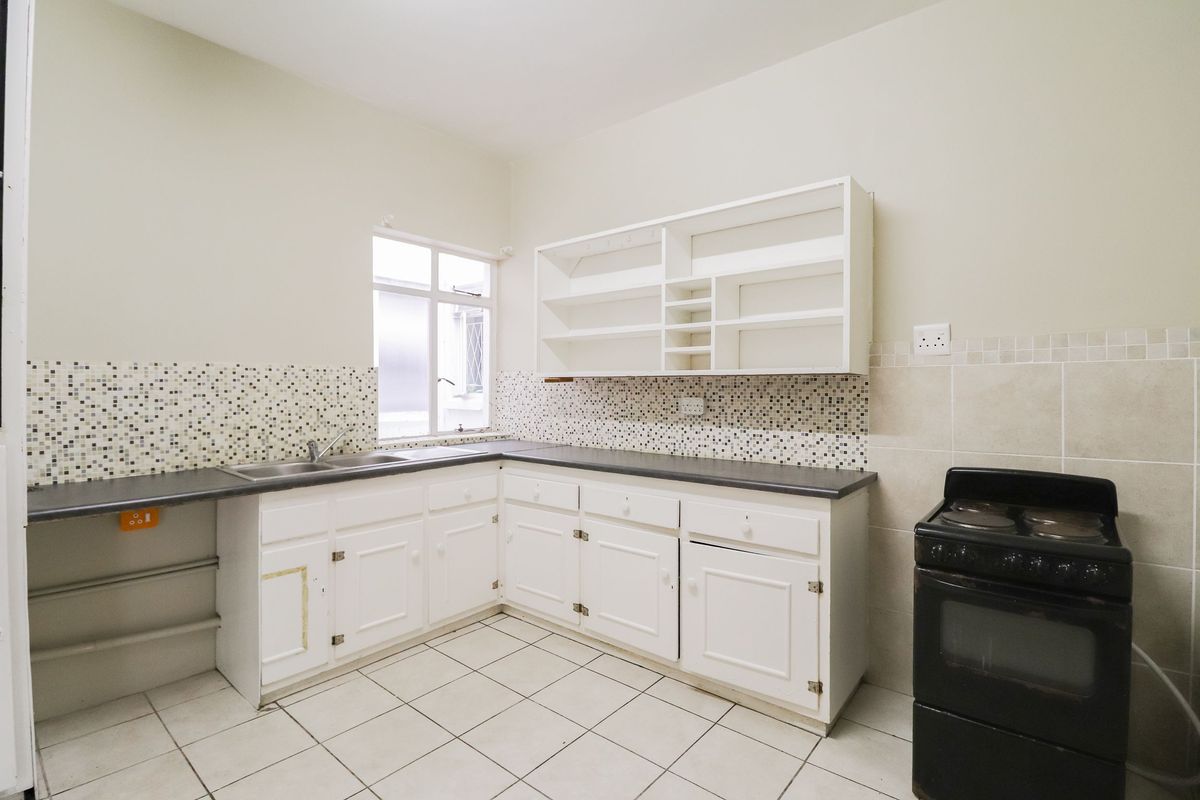 A functional kitchen featuring white cabinetry, dark countertops, a mosaic tile backsplash, and tiled flooring with a dedicated space for a freestanding stove.