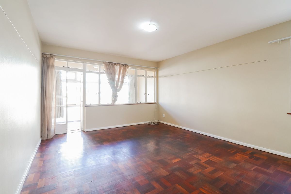 Spacious living room featuring original parquet flooring, neutral wall tones, and large windows providing natural light with direct access to an adjoining balcony.