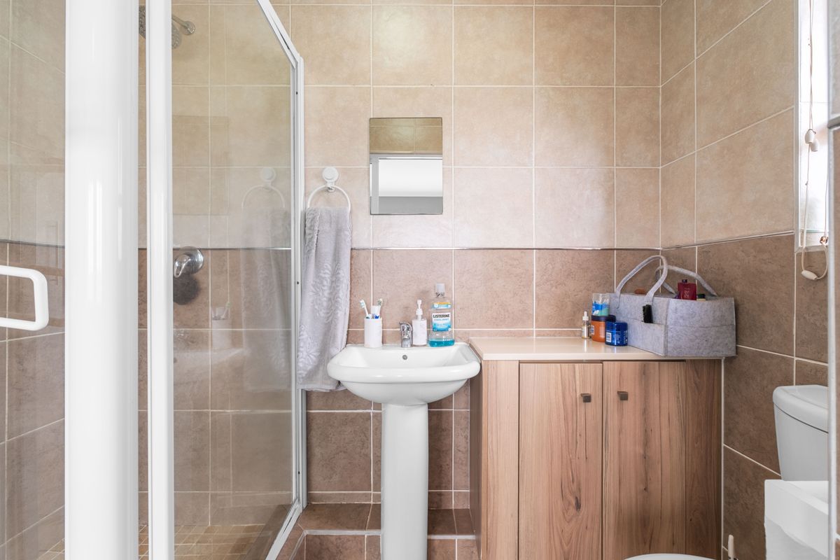 A functional bathroom featuring a glass-enclosed shower, pedestal basin, and built-in wooden vanity cabinet with tiled walls.