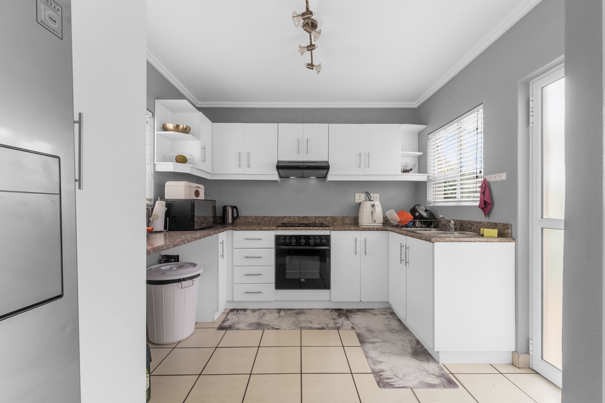 A functional kitchen featuring white cabinetry, granite-look countertops, a built-in oven with hob, extractor fan, and tiled flooring with direct outdoor access.