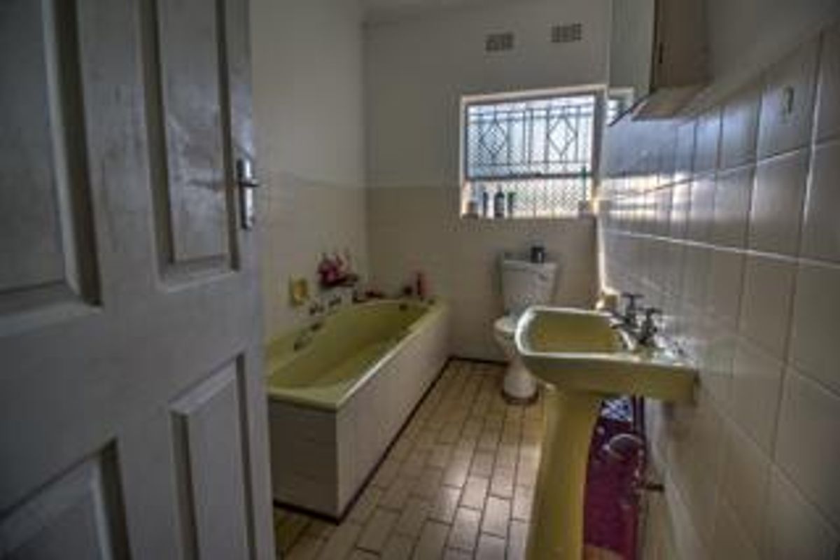 A dated bathroom featuring a pastel-colored bathtub and pedestal basin, tiled walls, and a window with security bars.