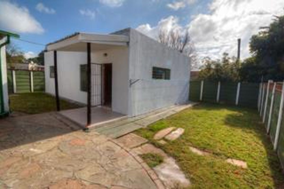 A view of the rear exterior of the house, featuring a covered patio area, paved sections, and a surrounding garden with boundary fencing.