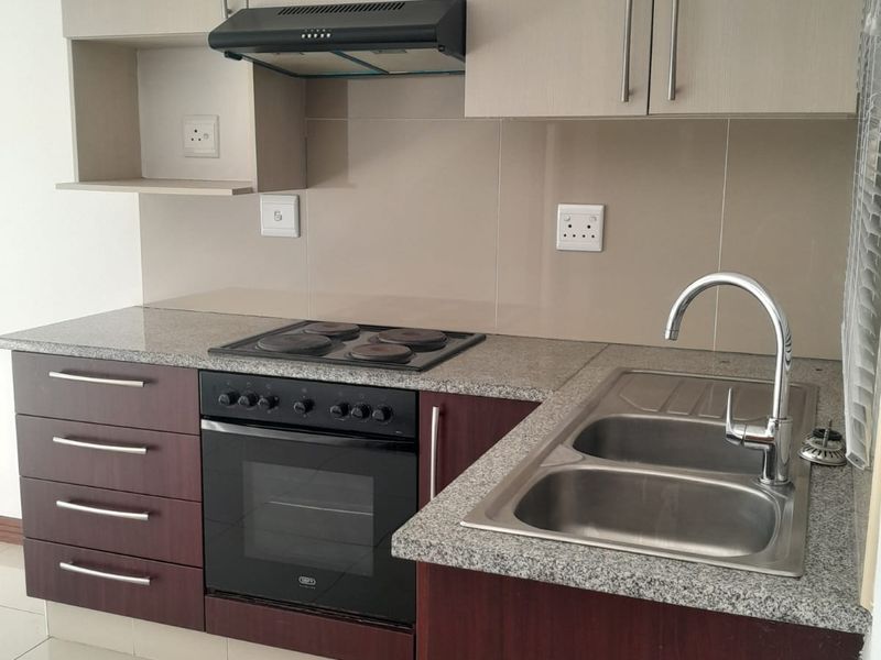 Compact kitchen featuring granite countertops, built-in oven, electric hob, extractor fan, and a double stainless steel sink with modern cabinetry.