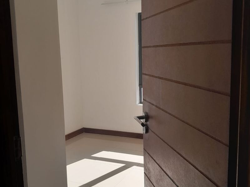 A bright, empty bedroom featuring tiled flooring, neutral walls, and a modern horizontal-slatted wooden door.