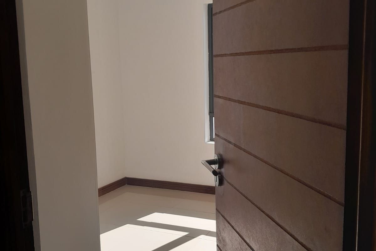 A bright, empty bedroom featuring tiled flooring, neutral walls, and a modern horizontal-slatted wooden door.