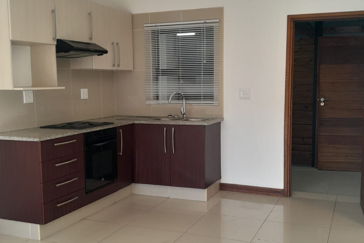 A compact kitchen featuring two-tone cabinetry, granite countertops, a built-in oven and hob, and tiled flooring in an open-plan layout.