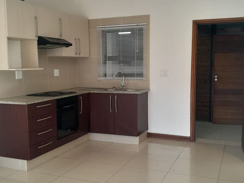 A compact kitchen featuring two-tone cabinetry, granite countertops, a built-in oven and hob, and tiled flooring in an open-plan layout.