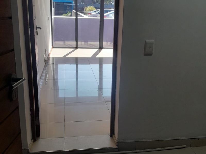 A view through a doorway into a bright, tiled living area featuring large glass sliding doors leading to an outdoor balcony.