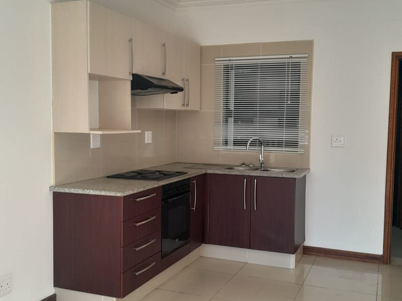 A compact, functional kitchen featuring two-tone cabinetry, a built-in oven, hob, extractor fan, and tiled flooring.