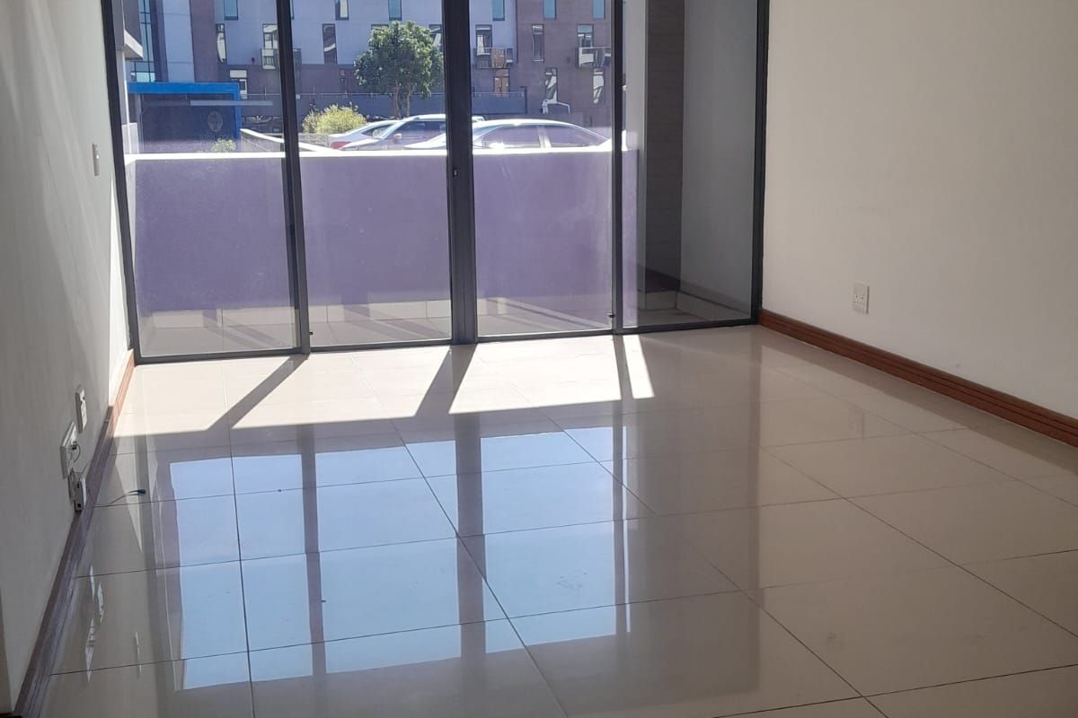 An empty, light-filled living area featuring large sliding glass doors that open onto a balcony, finished with neutral floor tiles.
