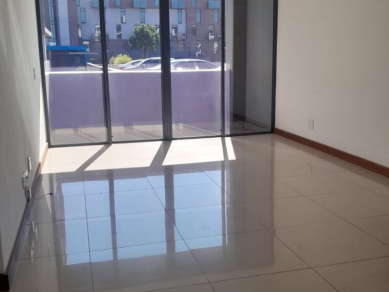 An empty, light-filled living area featuring large sliding glass doors that open onto a balcony, finished with neutral floor tiles.