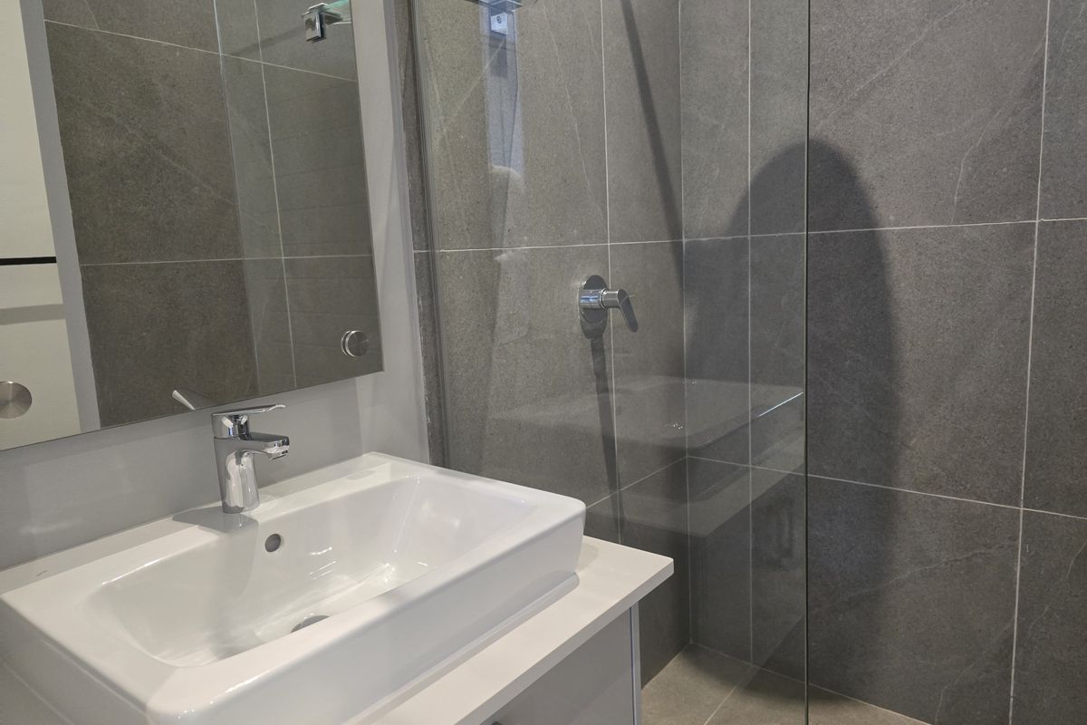 Modern bathroom featuring a sleek vanity with a white basin, a frameless glass shower enclosure, and contemporary grey wall and floor tiling.