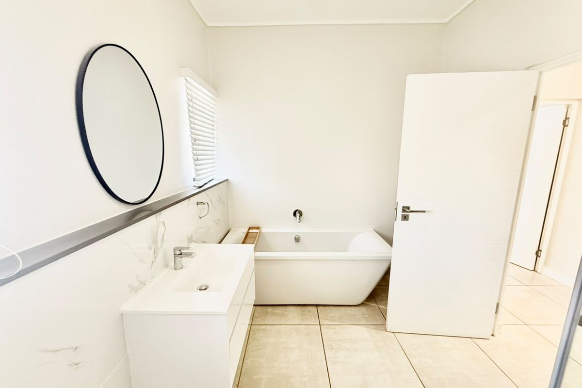 Modern bathroom featuring a sleek wall-mounted vanity, a contemporary freestanding bathtub, and neutral floor tiling with marble-effect wall accents.