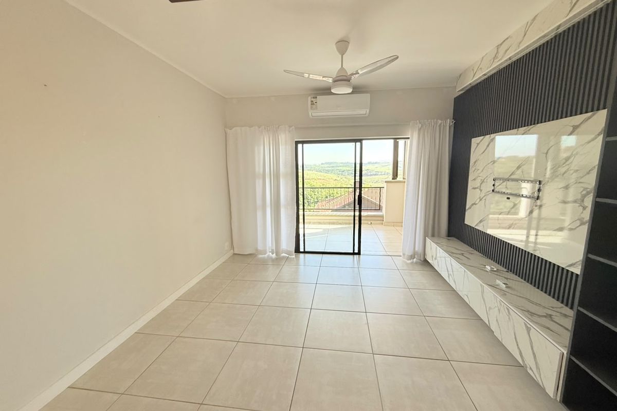 Spacious living area featuring large format floor tiles, a modern marble-look media wall with integrated shelving, ceiling fan, and sliding doors leading to a balcony.