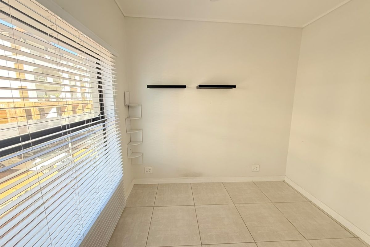 A bright, empty bedroom featuring neutral floor tiles, white walls, and fitted window blinds, offering a clean and versatile space.