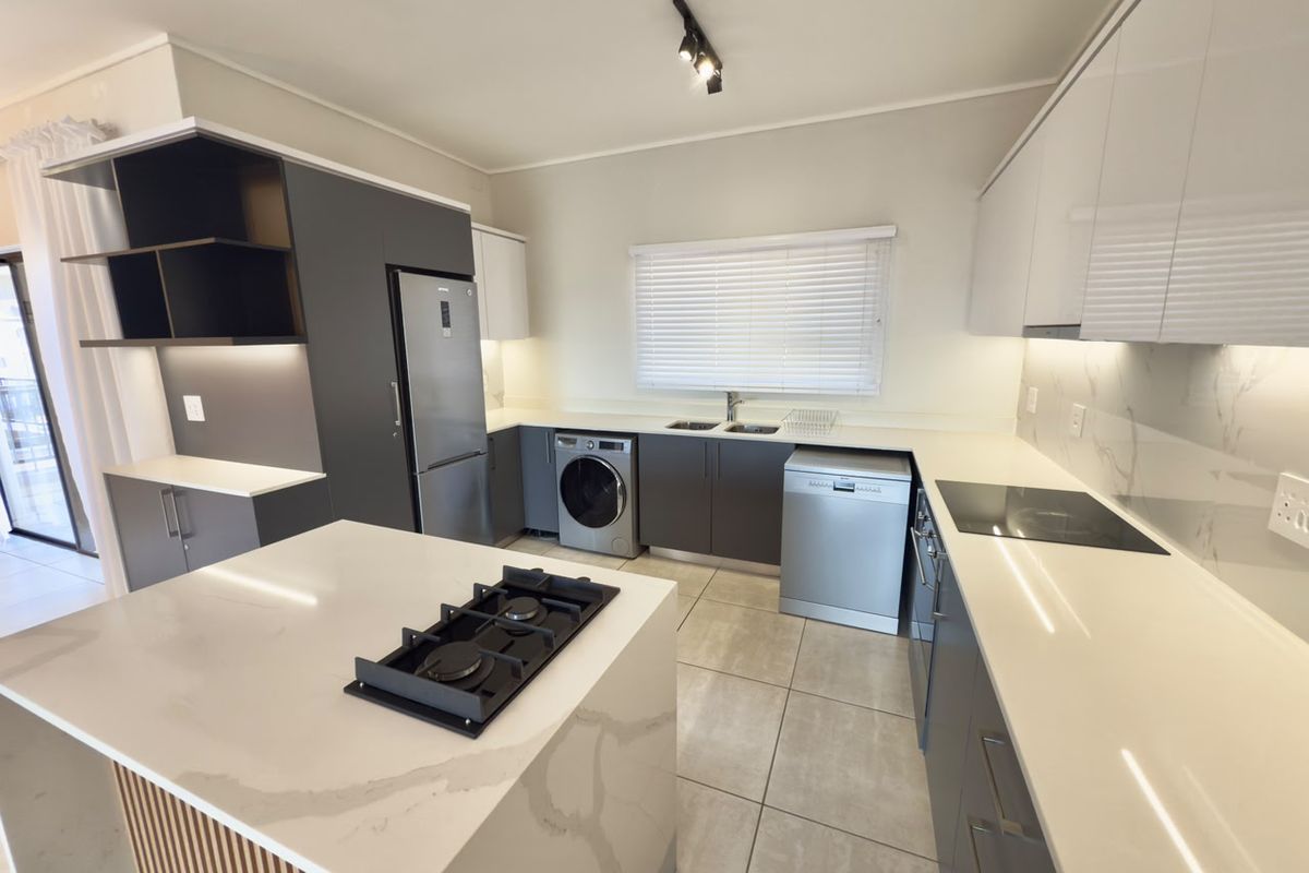 Modern kitchen featuring a central island with a gas hob, sleek cabinetry, stone countertops, and integrated appliance spaces.