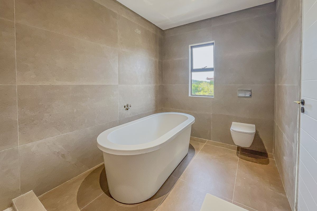 Modern bathroom featuring a freestanding bathtub, wall-mounted toilet, and large format neutral floor-to-ceiling tiles.