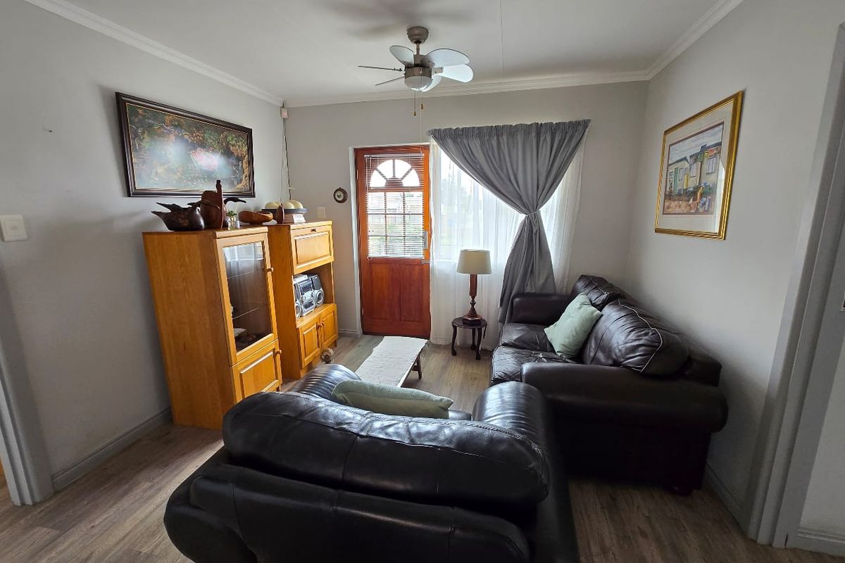 A cozy living room featuring wood-look laminate flooring, a ceiling fan, and a wooden entrance door with glass paneling.