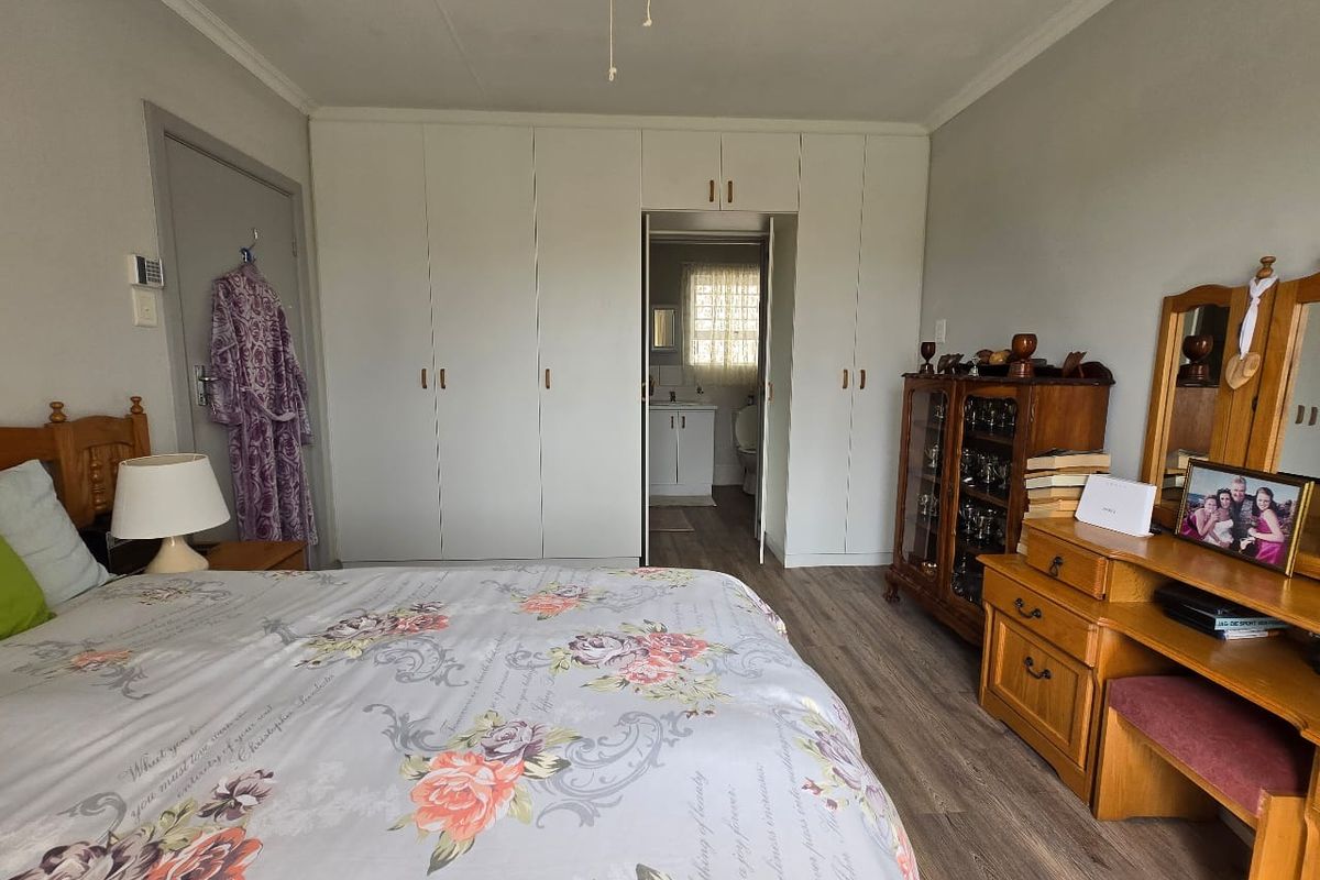 A well-maintained bedroom featuring built-in floor-to-ceiling wardrobes, wood-look laminate flooring, and direct access to an en-suite bathroom.