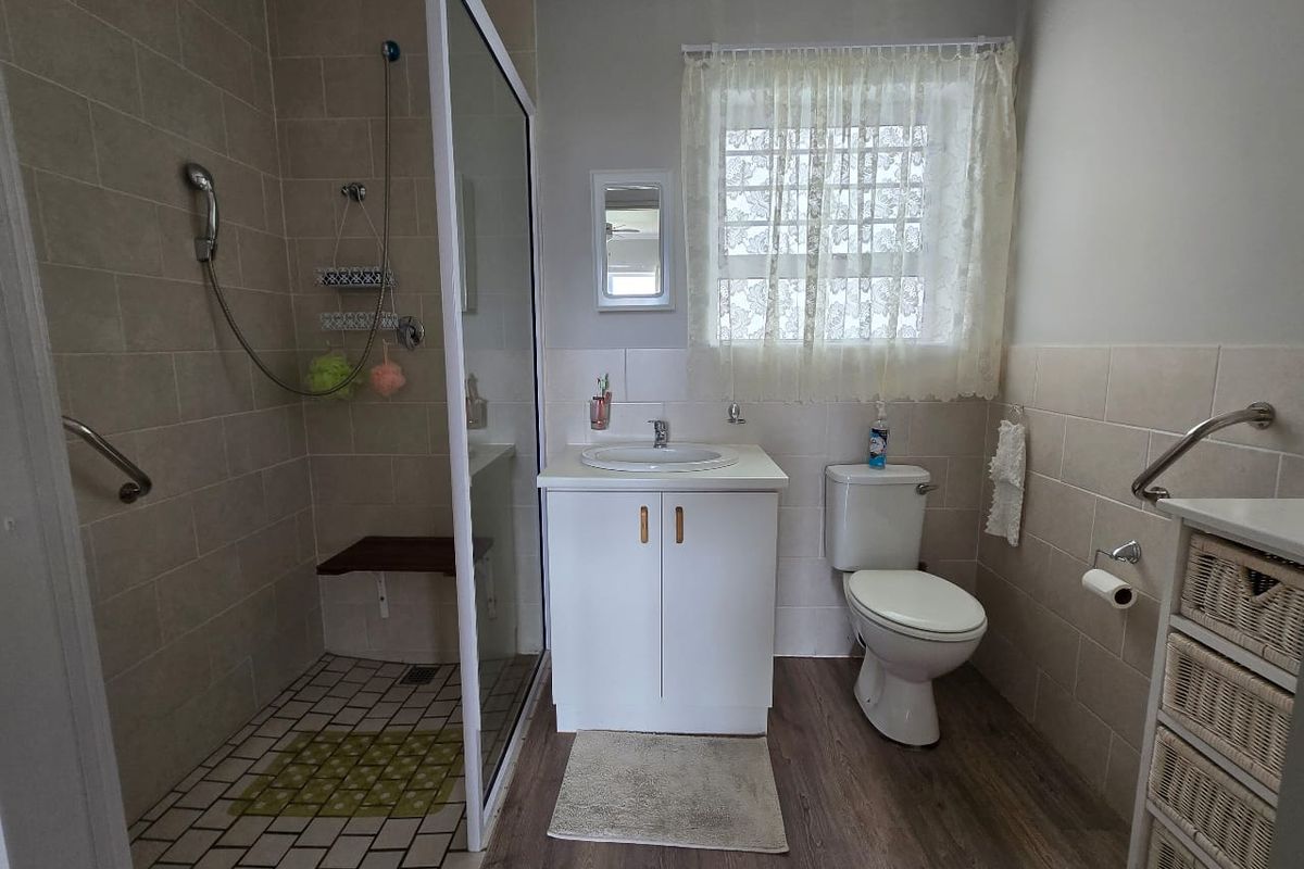 A functional bathroom featuring a walk-in shower with a built-in seat, a vanity basin, and a toilet, finished with neutral wall tiling.