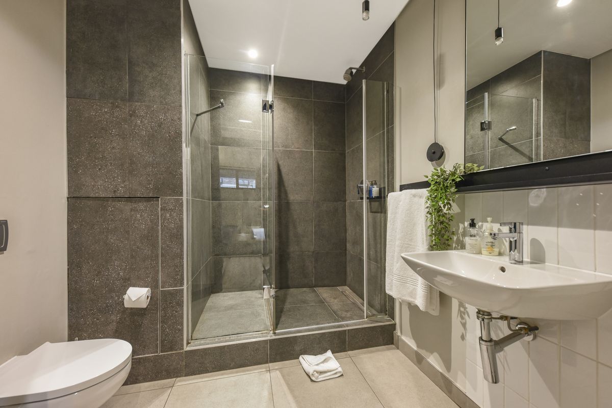 Modern bathroom featuring a walk-in glass shower with dark stone tiling, a wall-mounted basin, and a contemporary toilet.