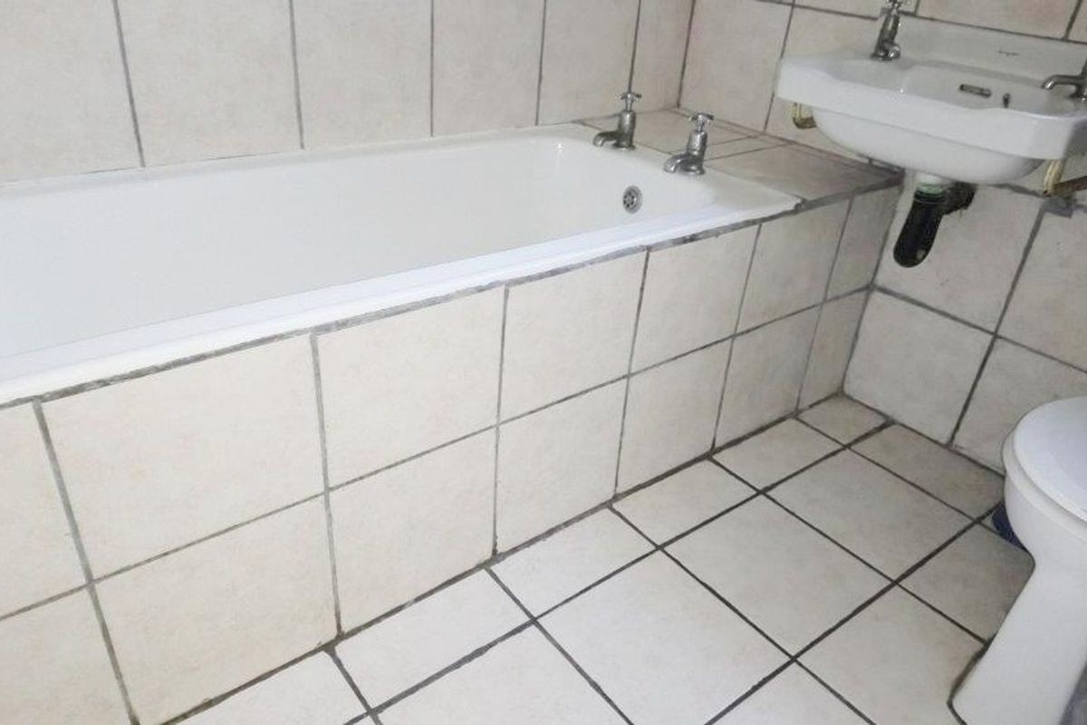 A functional bathroom featuring a built-in bathtub, pedestal basin, and toilet with neutral floor and wall tiling.