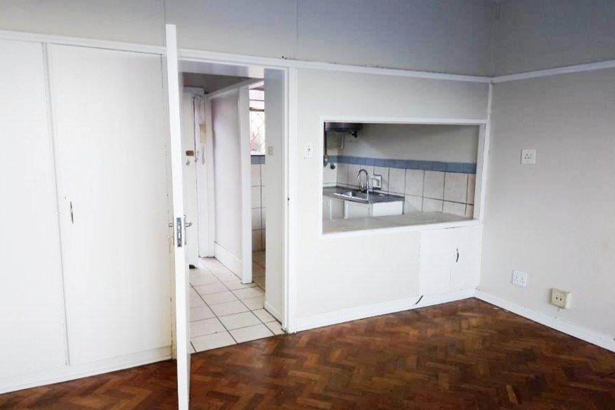 A view from the living area into the kitchen, featuring original parquet flooring, built-in cupboards, and a serving hatch window.