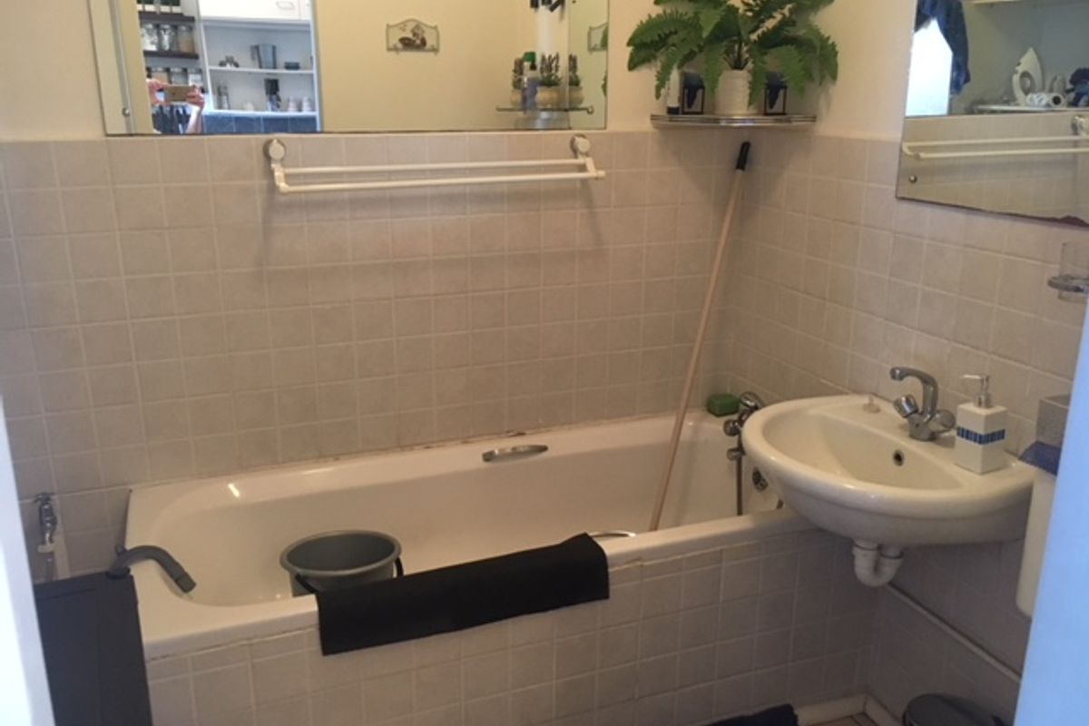 A functional bathroom featuring a standard bathtub, wall-mounted basin, and tiled splashbacks with a large vanity mirror.