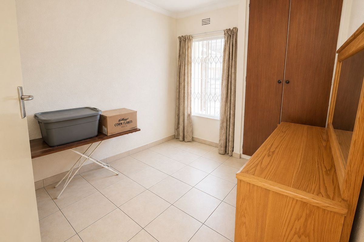 A bedroom featuring tiled flooring, built-in wooden cupboards, and a window with security bars.