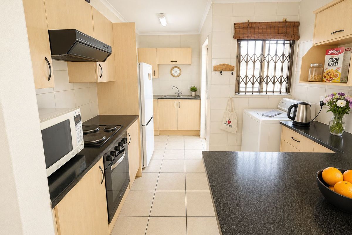 A functional kitchen featuring light wood cabinetry, dark countertops, tiled flooring, and a built-in oven with an extractor fan.