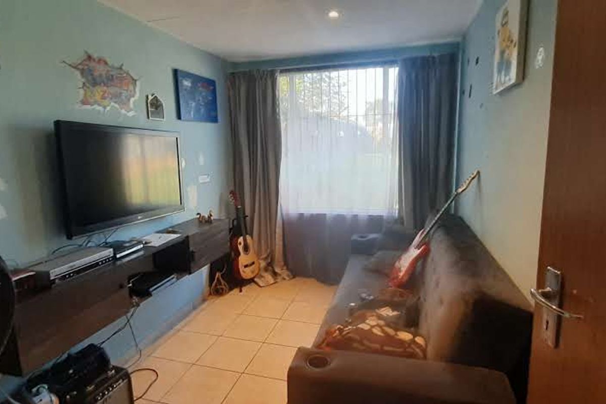 A compact living room featuring tiled flooring, a wall-mounted media console, and a large window with security bars.