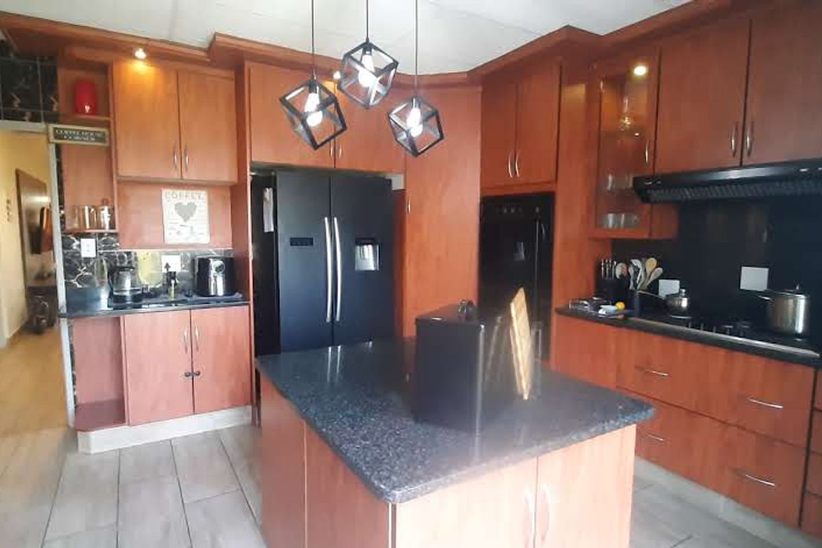 A functional kitchen featuring warm-toned wooden cabinetry, a central island with a dark countertop, and integrated black appliances.