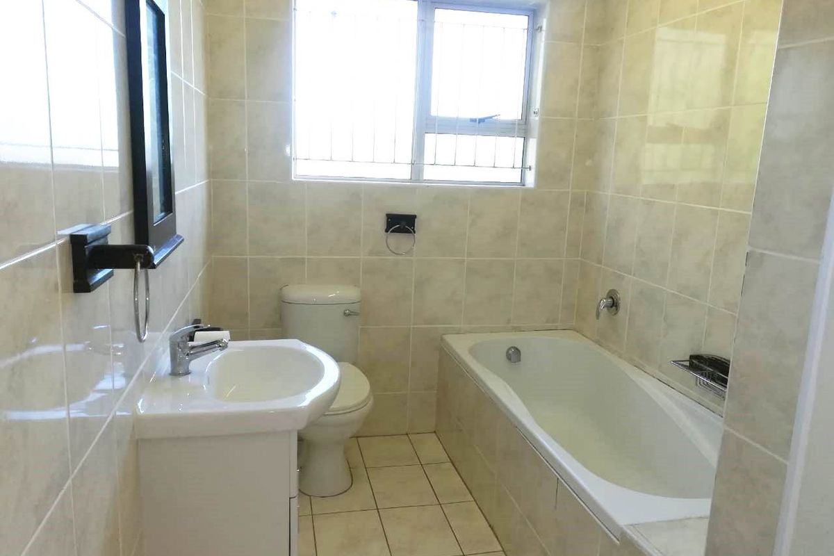 A functional bathroom featuring a bathtub, toilet, and vanity basin with neutral wall and floor tiling.