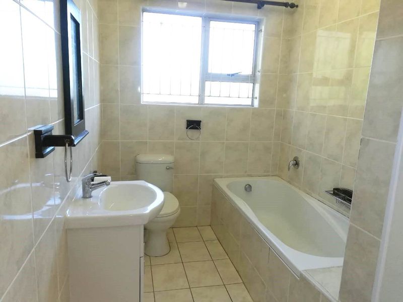 A functional bathroom featuring a bathtub, toilet, and vanity basin with neutral wall and floor tiling.
