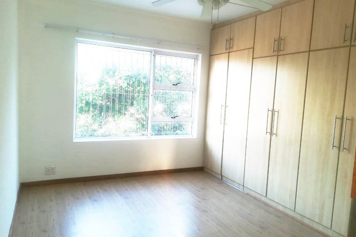 A bright, empty bedroom featuring light wood-look laminate flooring, extensive built-in cupboards, and a ceiling fan.