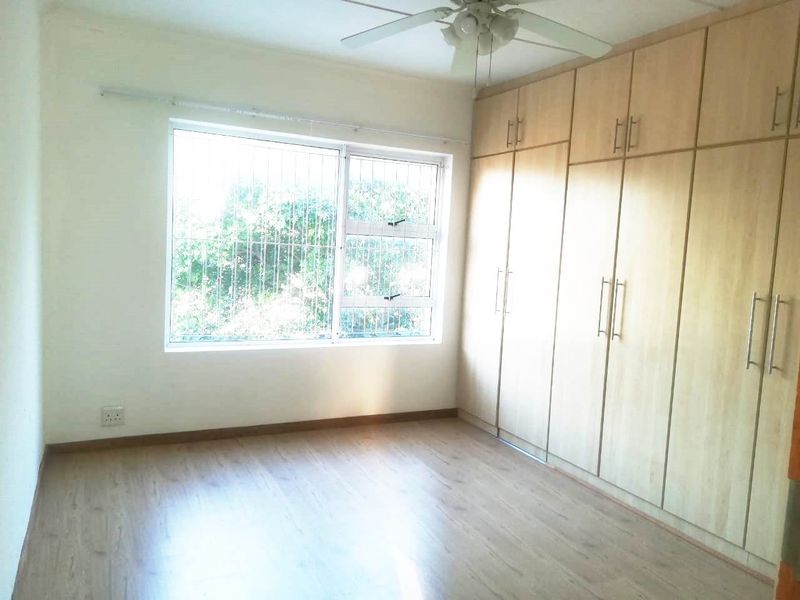 A bright, empty bedroom featuring light wood-look laminate flooring, extensive built-in cupboards, and a ceiling fan.