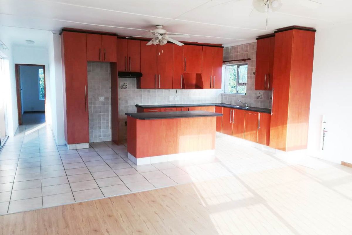 Spacious open-plan kitchen featuring wood-finish cabinetry, a central island, tiled backsplash, and integrated sink, offering a functional layout for modern living.