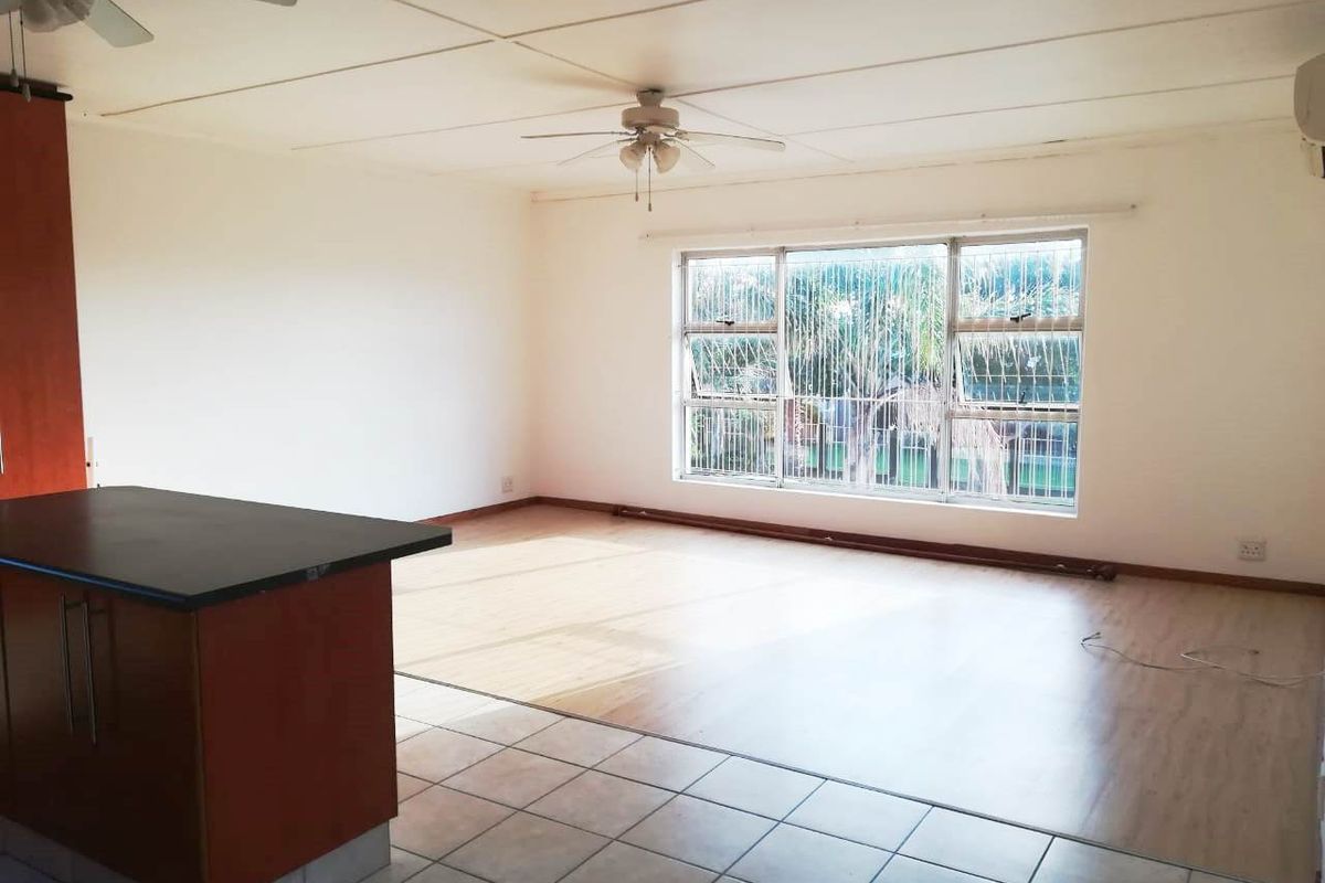 Spacious open-plan living area featuring a kitchen island, dual flooring finishes, ceiling fans, and large windows with security bars.